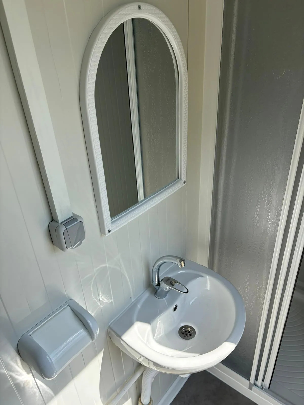 Interior of a portable bathroom unit with sink, mirror, and toilet roll holder.