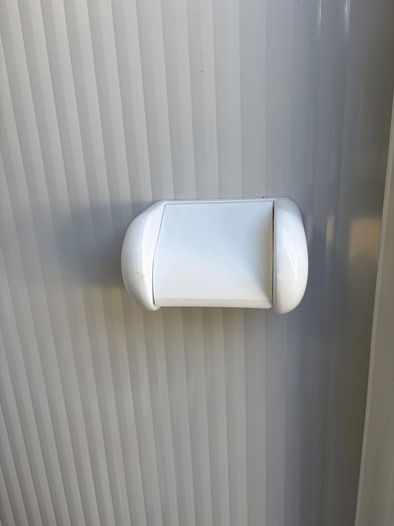 Toilet roll holder inside a portable toilet unit for camping.